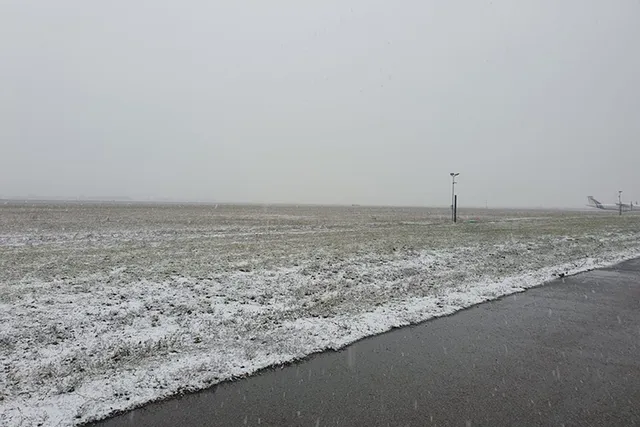 Platformă aeroportuară acoperită de zăpadă, cu o aeronavă vizibilă în fundal