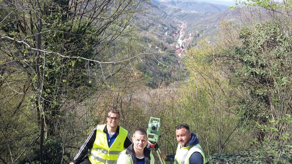 Trei colegi din echipa PROMETER M&G, pe un versant împădurit, cu o localitate vizibilă în vale